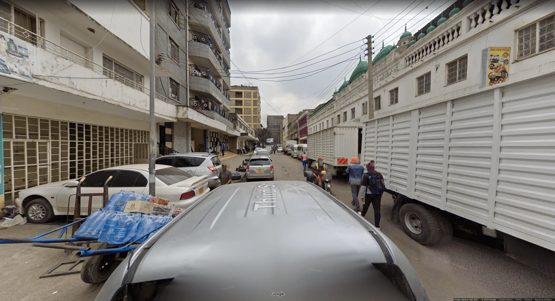 Picture taken on top of a car in a small, dusty alleyway. There is Arabic script on the right-hand side, and the license plates are yellow. Left-hand drive is also present